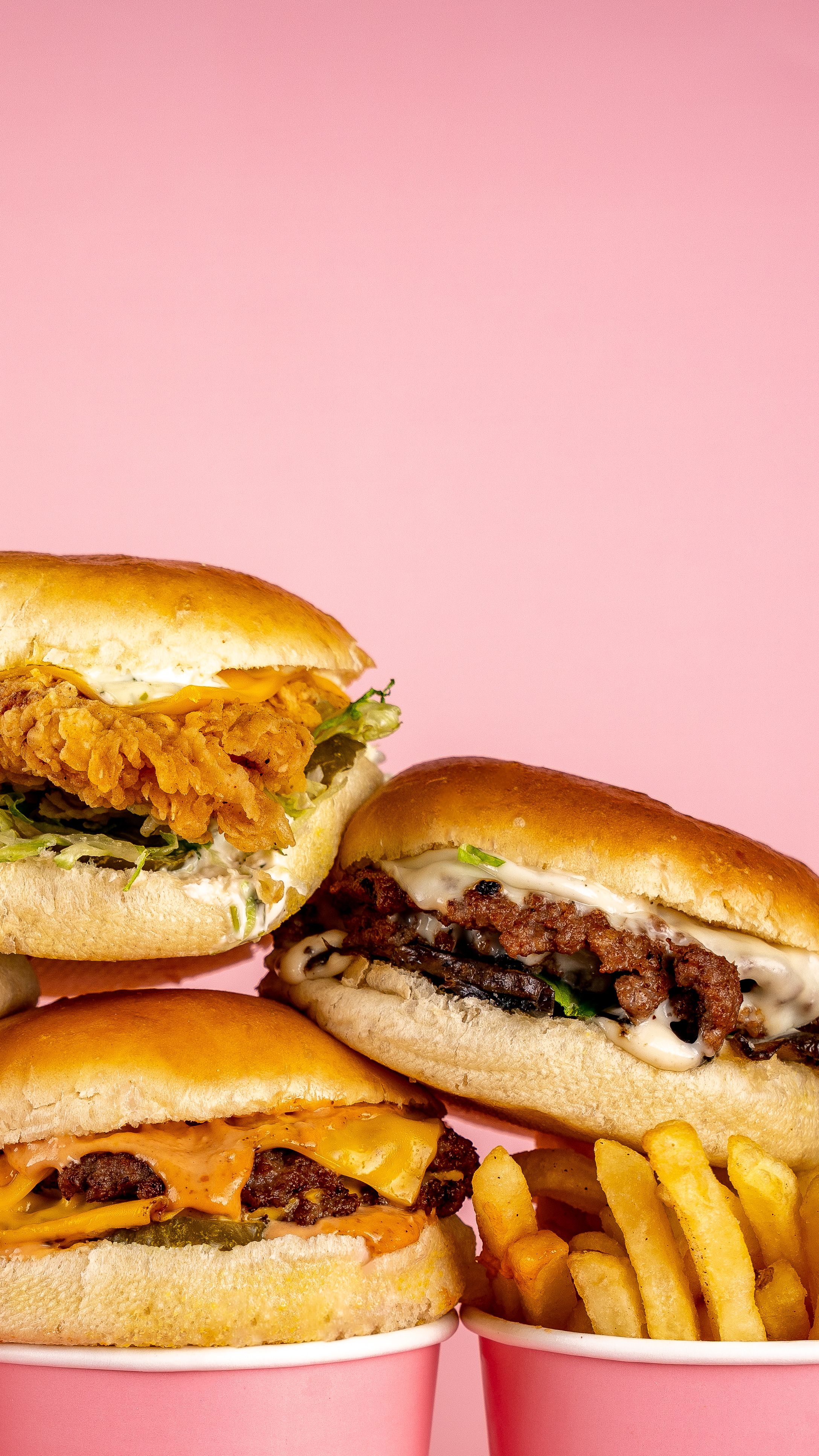 Burgers, a crispy chicken sandwich, and fries against a pink background